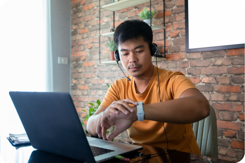 A person looking at his watch while working in front of a laptop.